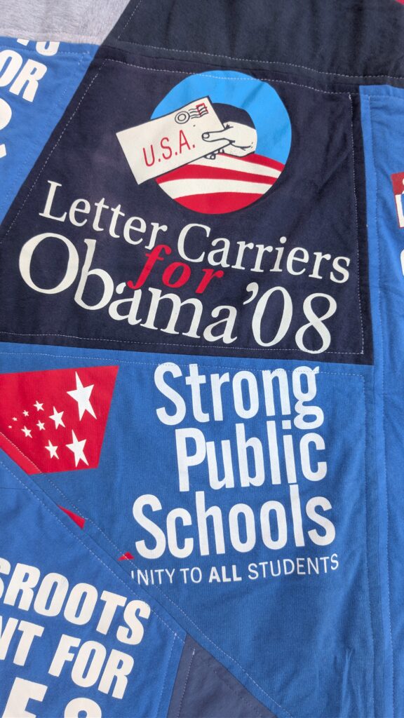 A patchwork of blue, white, and dark blue fabric features political slogans and imagery. One section reads "Letter Carriers for Obama '08" with a graphic of a hand holding a U.S.A. envelope. Another section says "Strong Public Schools" and "unity to all students." A third section has "ROOTS NT FOR" in large white letters.