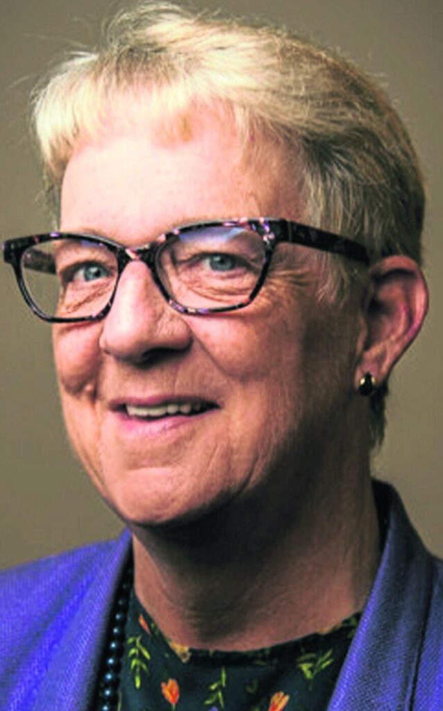 A close-up portrait of a person wearing glasses and a purple jacket.