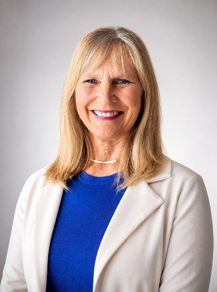 A headshot of a smiling, blonde woman wearing a blue shirt and a cream-colored blazer.