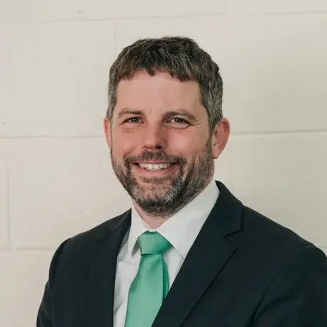A man in a dark suit and green tie smiles at the camera.