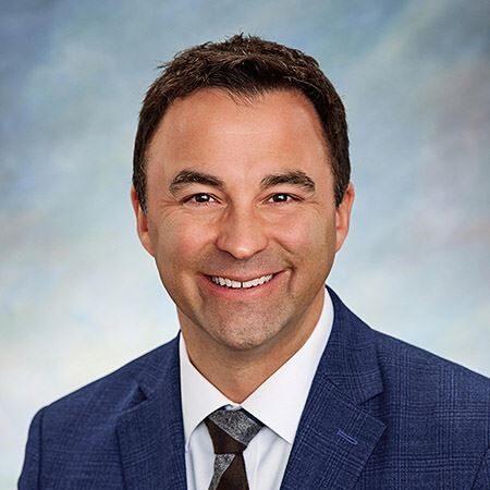 A man in a blue suit and tie smiles at the camera.