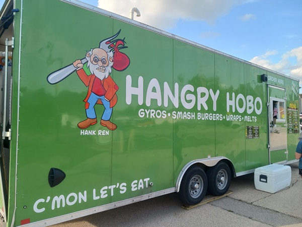 A green food truck named "Hangry Hobo" with a cartoon character of a hobo holding a fork. The truck advertises gyros, smash burgers, wraps, and melts.