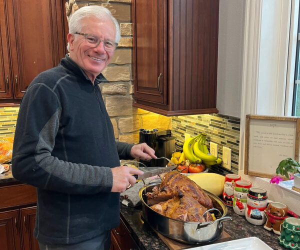 Rick Dickinson smiles in a home kitchen while carving a roasted turkey.