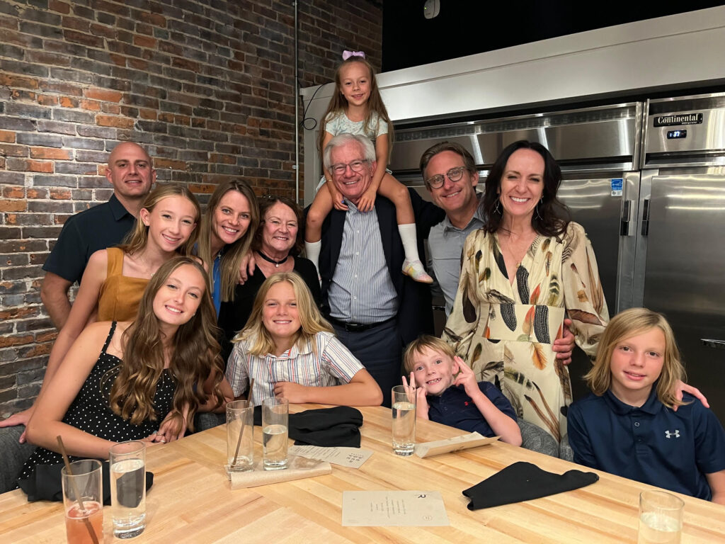 A large family poses for a photo in front of a brick wall and a stainless steel refrigerator.